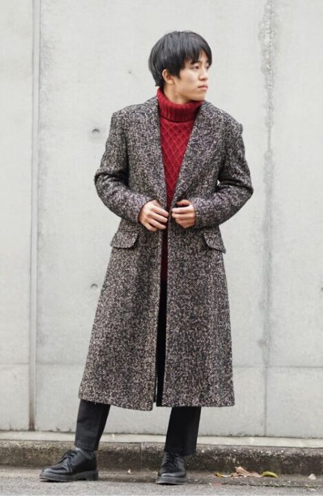 赤色のセーターの上にグレーのロングコートを着た男性