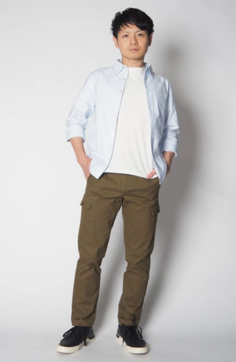 白いカットソーの上に淡い水色のシャツをはおり、カーキ色のカーゴパンツをはいた男性