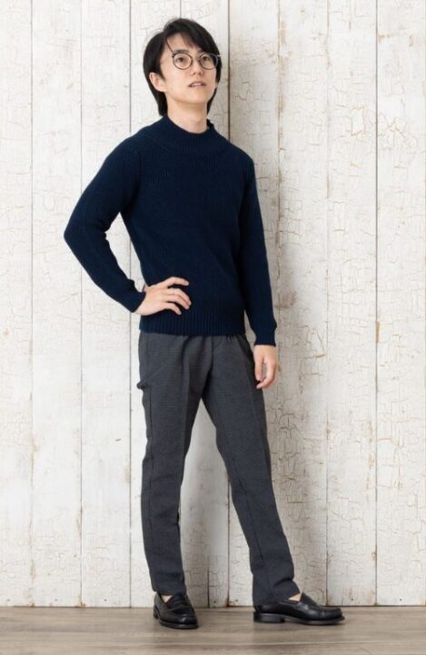 黒い長袖カットソーとグレーのパンツ、黒い革靴を着用した男性