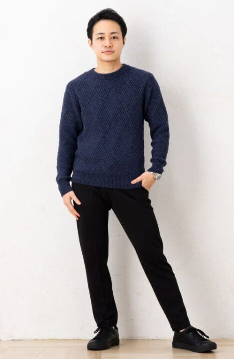 編み目が入ったネイビーのセーターと黒いパンツを着用した男性