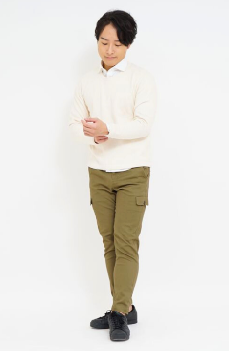 白いシャツの上にオフホワイトのセーターを着用し、カーキ色のカーゴパンツをはいた男性