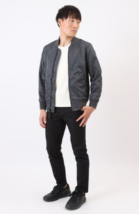 白いカットソーの上に濃いグレーのブルゾンをはおり、黒いパンツをはいた男性