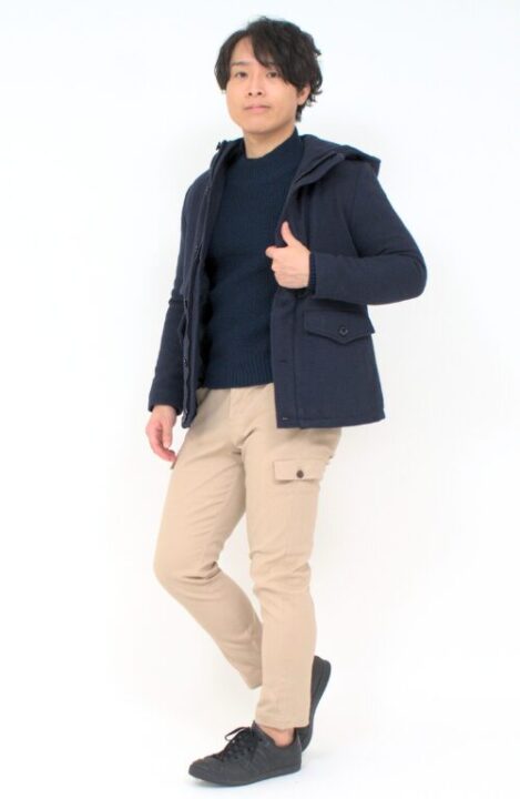 ネービーのセーターの上にショートコートをはおり、ベージュのカーゴパンツを着用した男性