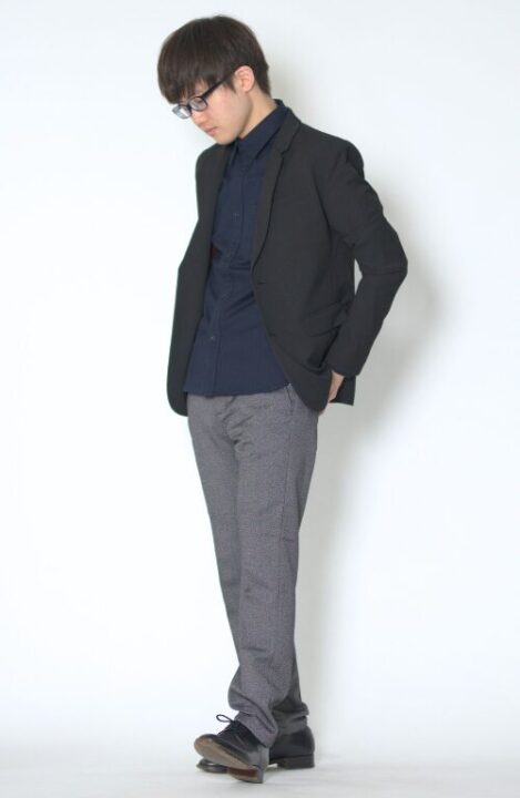 ネイビーのシャツの上に黒いジャケットをはおり、グレーのパンツをはいた男性
