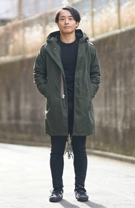 黒いカットソーの上にモッズコートをはおり、道端にたたずむ男性