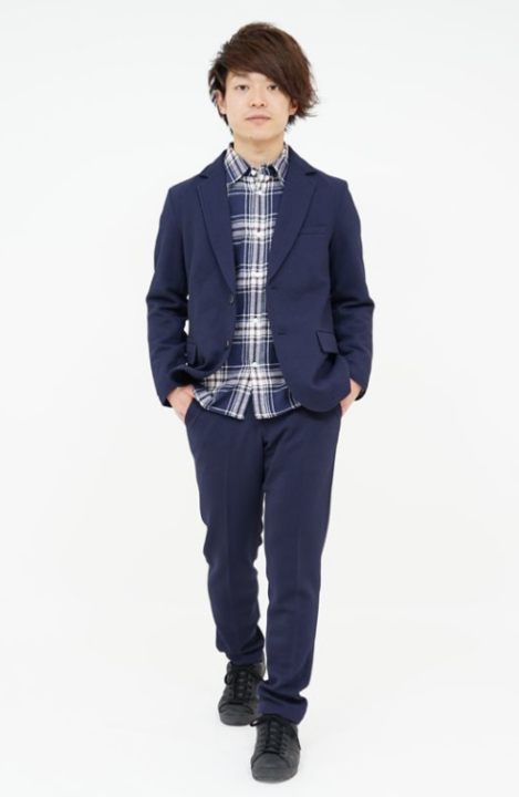 青色のチェック柄シャツの上にネイビーのジャケットをはおり、ネイビーのパンツを着用した男性