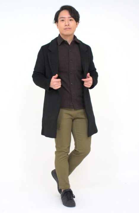 ブラウンのシャツの上に黒色のチェスターコートをはおり、カーキ色のカーゴパンツを着用した男性