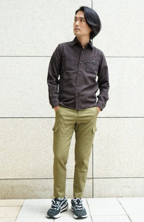 茶色のシャツとカーキ色のカーゴパンツを着用し、ボリュームのあるスニーカーを履いた男性