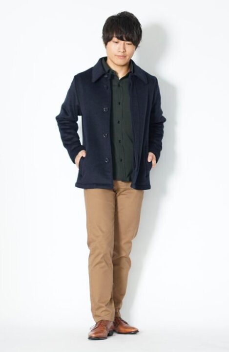 黒いシャツの上にネイビーのPコートをはおり、茶色のパンツと靴をはいた男性